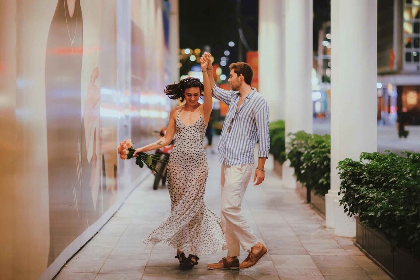 A couple walking hand in hand on a tiled sidewalk at night. 1