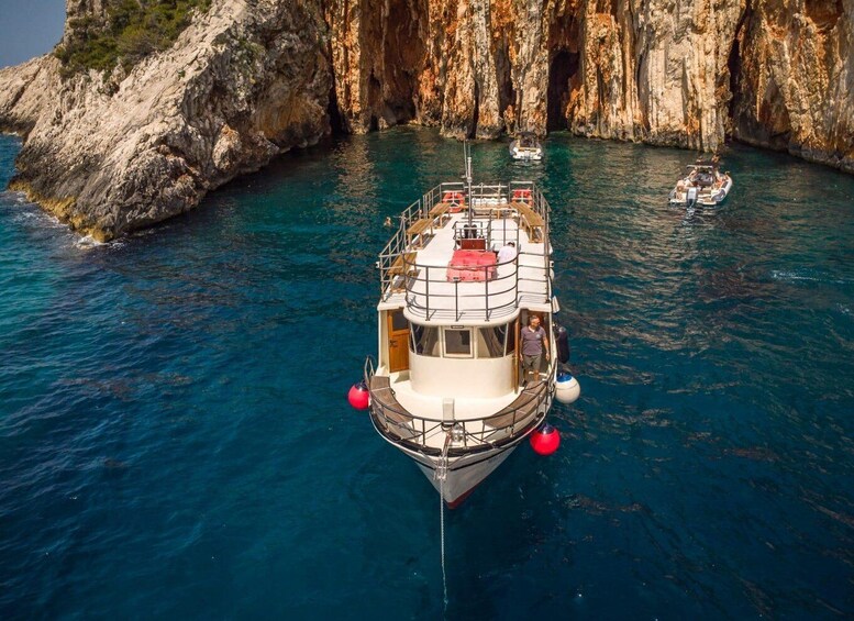 A boat anchored near a rocky coastline with clear blue water. 3