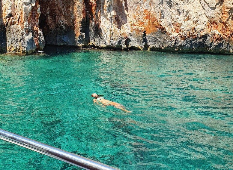 A person swimming in clear turquoise water near rocky cliffs. 4
