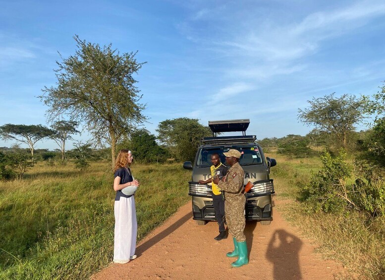 A safari vehicle with an open roof, two people standing beside it, and a woman walking on a dirt path in a savannah landscape. 4