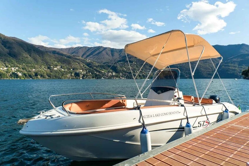 A boat named 'Altea Lake Com Boat-Ol' docked at a wooden pier with a mountainous backdrop. 1