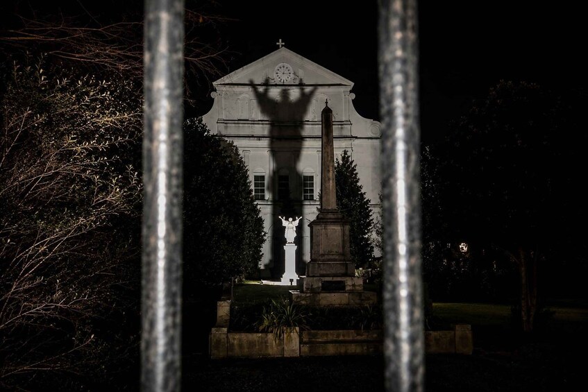 A white building with a clock and a statue in front, surrounded by trees. 1
