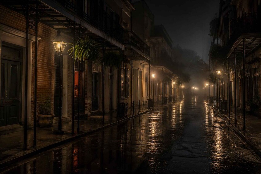 A wet street at night with buildings on either side and street lamps. 2