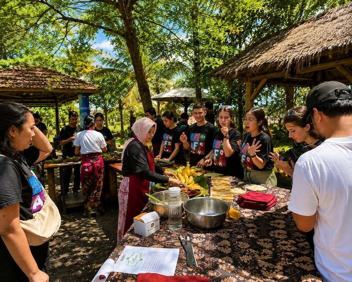 A group of people gathered around a table with food items, possibly at an outdoor event or market. 2
