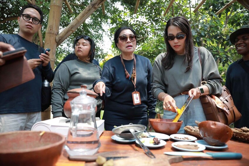 A group of people around a table with food and cooking utensils, outdoors with trees in the background. 4