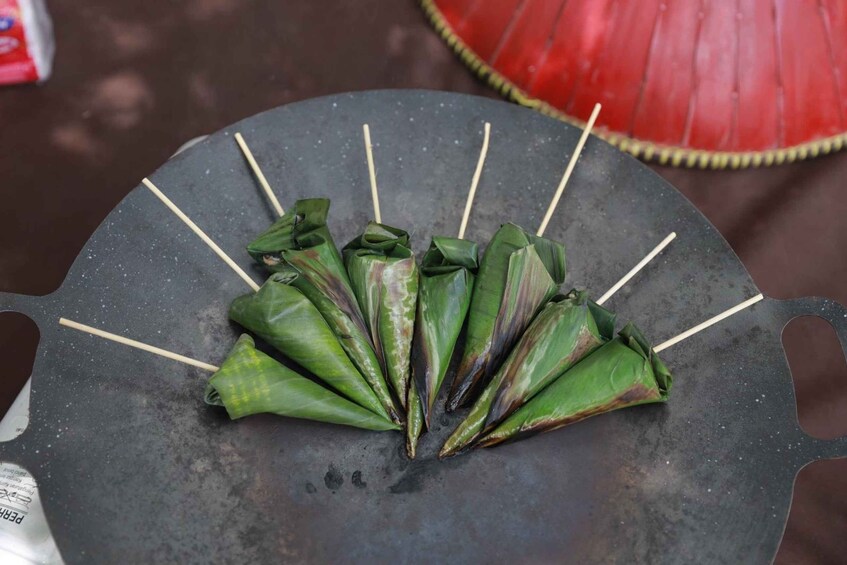 A black tray with several green banana leaves tied with sticks, likely for cooking. 3
