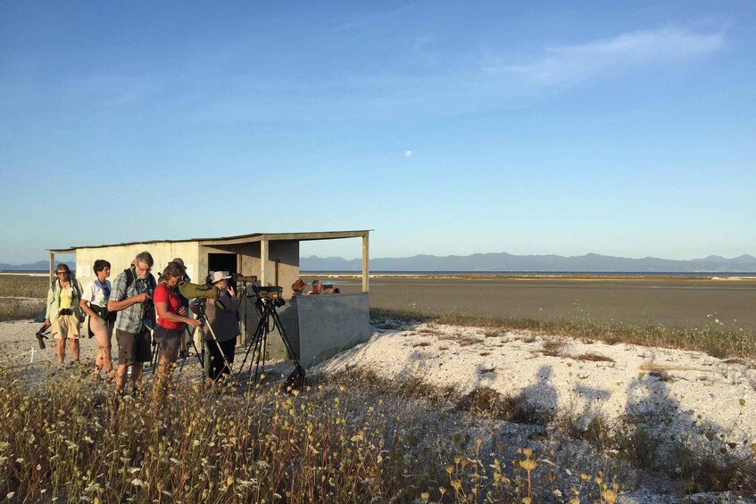 A group of people near a small structure on a beach with mountains in the background. 1