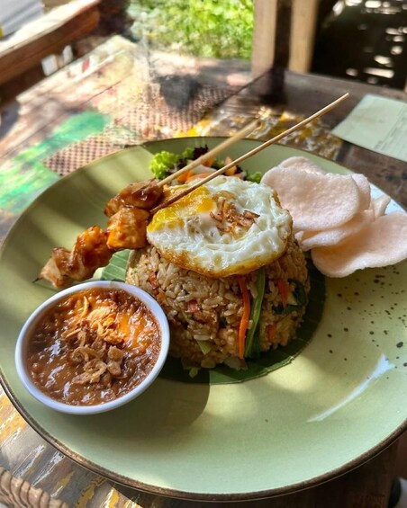 A plate of fried rice with a fried egg, skewers, and a small bowl of sauce. 3