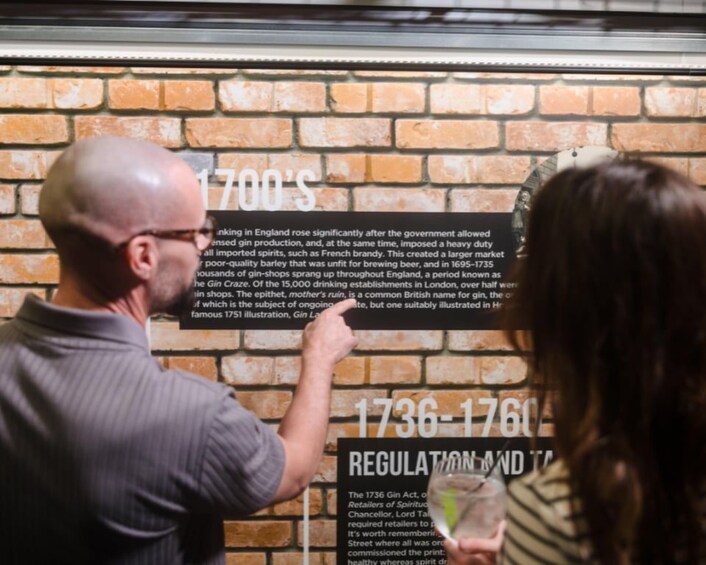 A man and a woman reading a historical sign about gin in England. 2