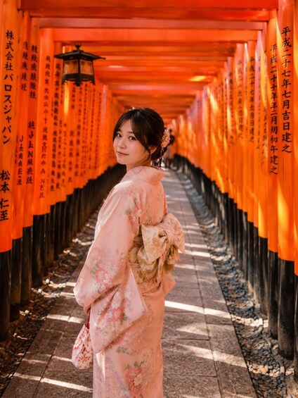 A person in traditional attire walking through a corridor lined with orange torii gates. 5