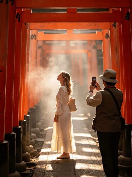A person taking a photo of a person in a white dress at a traditional Japanese torii gate. 1