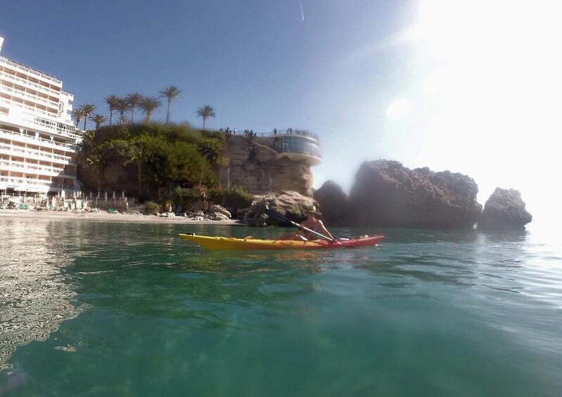 A kayaker on a calm sea with a cruise ship and rocky cliffs in the background. 2