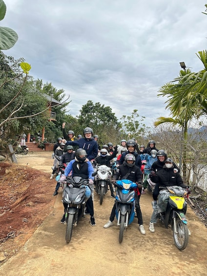 A group of motorcyclists on a dirt path with trees and a building in the background. 3