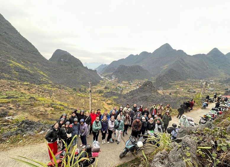A group of people gathered on a mountain path with a valley and mountains in the background. 4