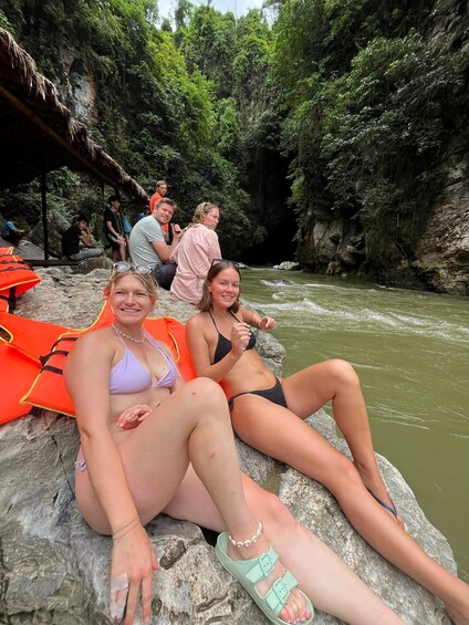 Two people sitting on a rock by a river surrounded by greenery. 2
