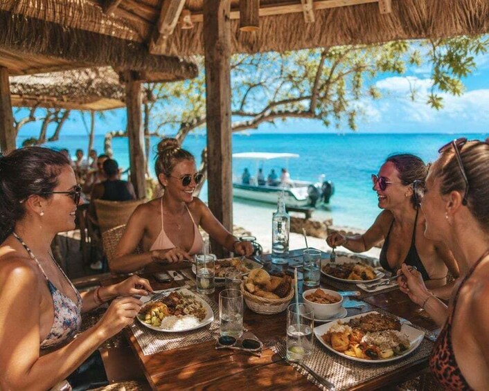 A group of people dining at an outdoor table with a view of the ocean and a boat in the background. 4