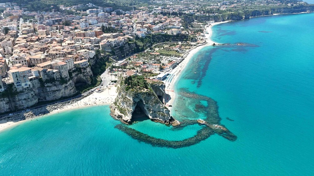 An aerial view of a coastal town with a prominent cliffside, a beach, and clear turquoise waters. 2