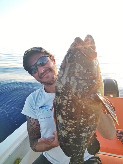 A person holding a large fish with a boat in the background. 5