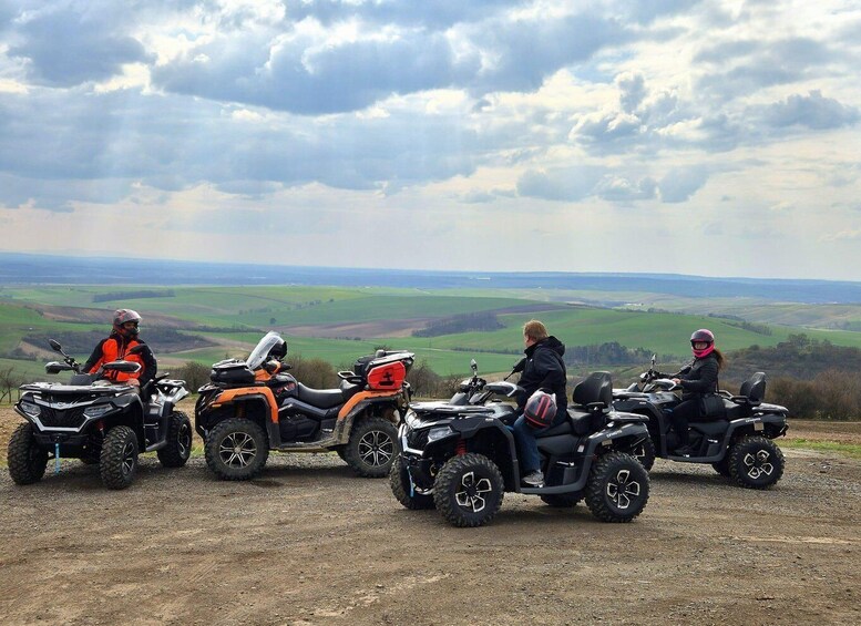 Four quad bikes parked on a dirt path with a scenic view of rolling hills and a cloudy sky. 1