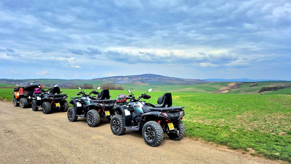 Four ATVs parked on a dirt path with a rural landscape in the background. 2