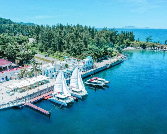 A marina with sailboats docked, a pier, and a forested coastline. 1