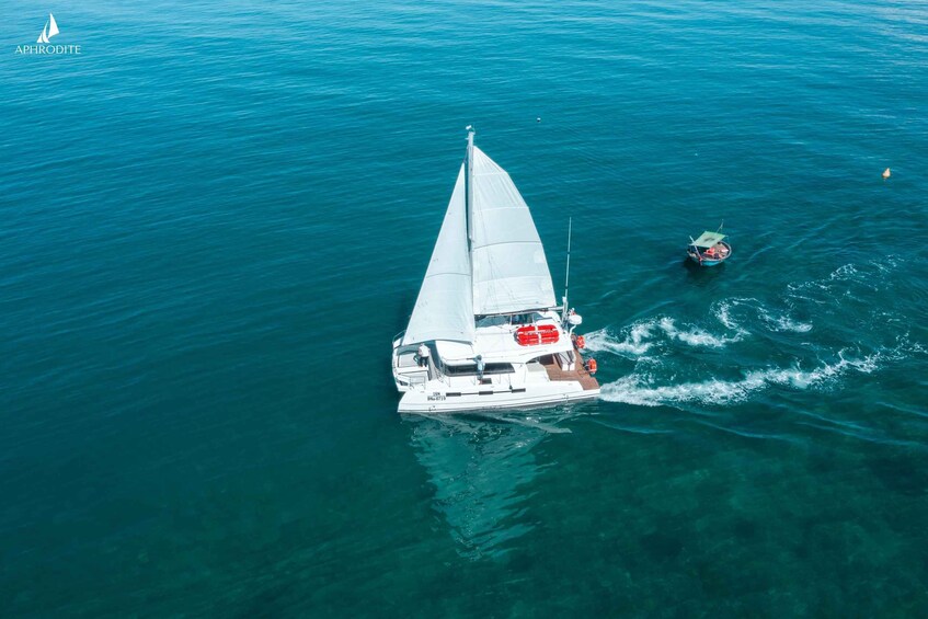 A sailboat with a white sail and a smaller boat nearby in clear blue water. 5