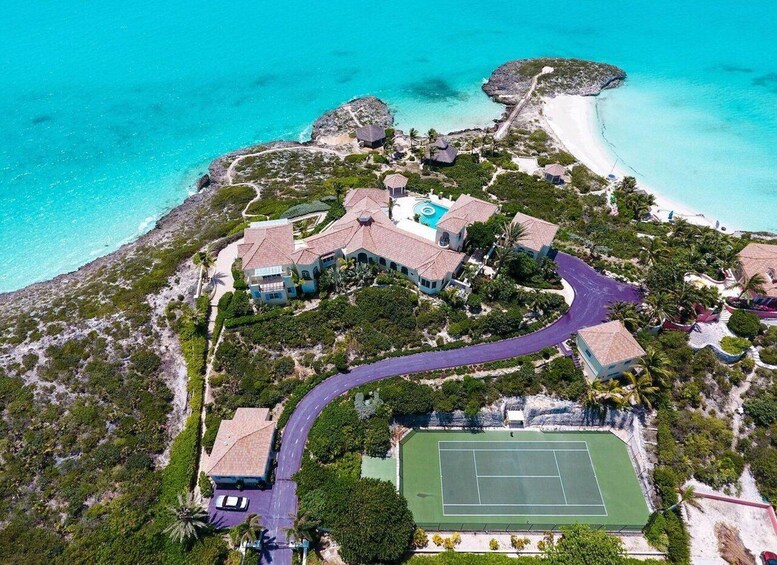An aerial view of a resort with multiple buildings, a tennis court, and a beach. 3