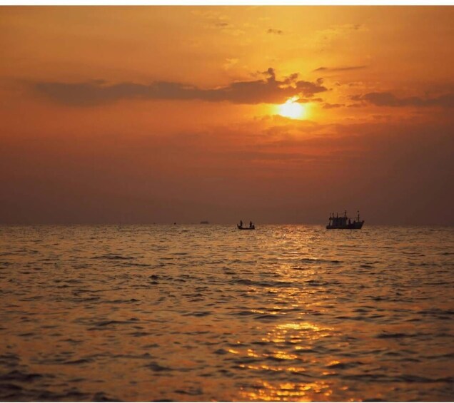 A sunset over a calm sea with a boat and a larger ship in the distance. 4