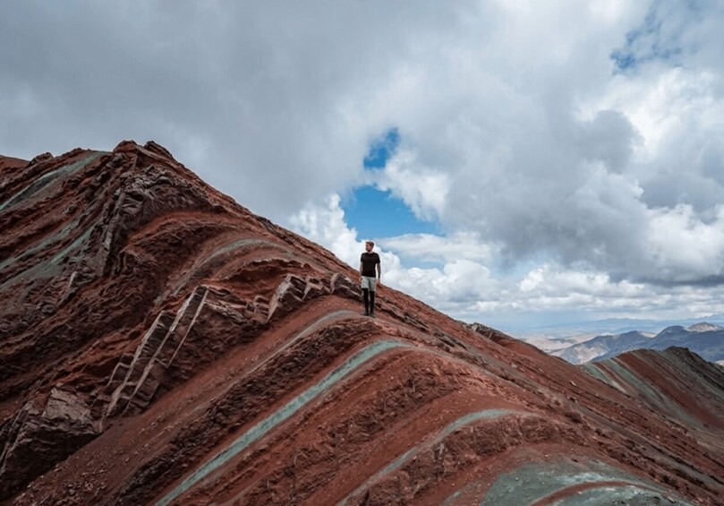 A person standing on a red and green striped mountain with a ladder, under a cloudy sky. 5
