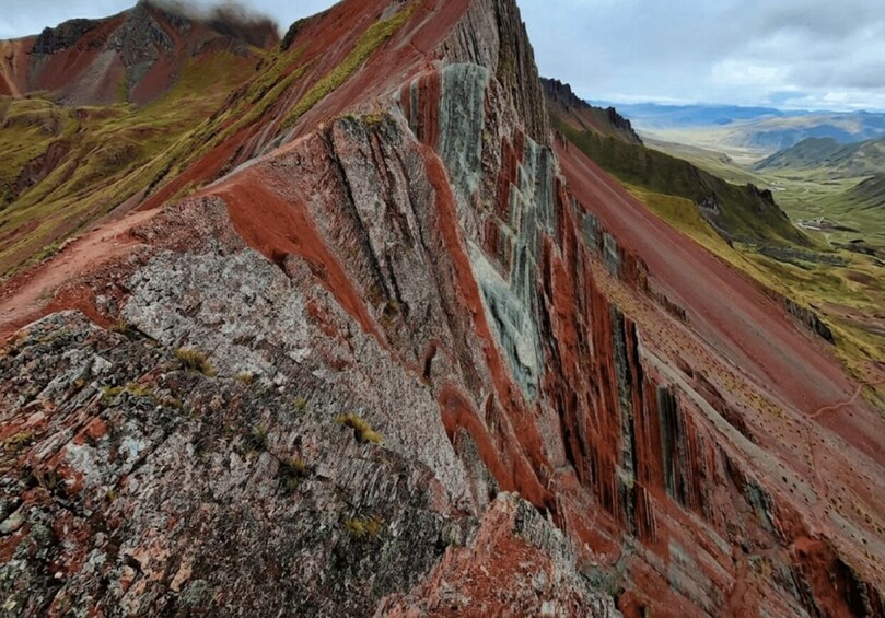 A rugged mountain landscape with distinct red and green stratified rock formations. 4