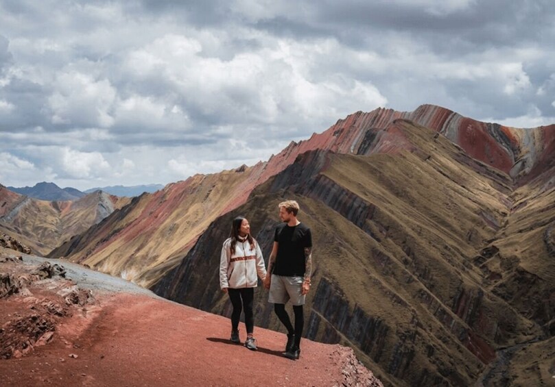 Two people walking on a red path in a mountainous area with colorful rock formations. 3