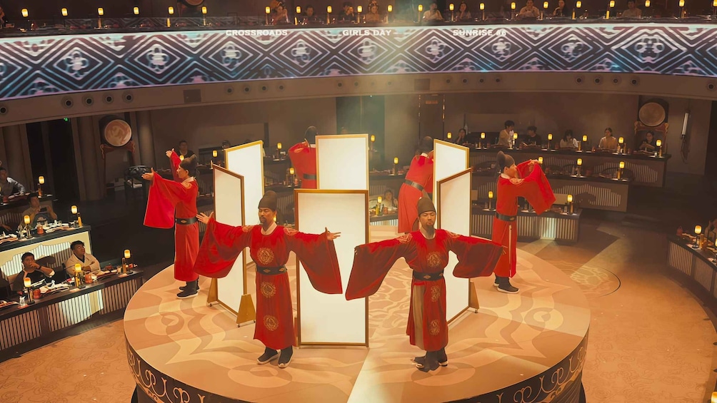 A stage with performers in red costumes, a patterned ceiling, and a seated audience. 2