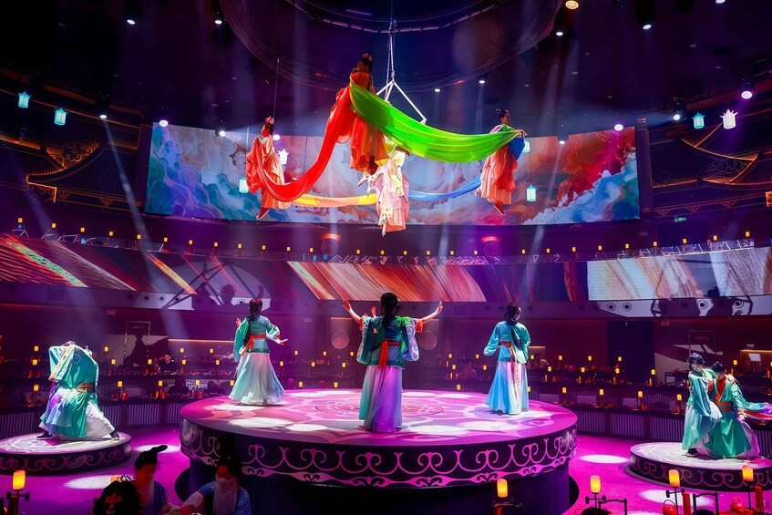 A stage with performers in traditional costumes, a large screen in the background, and a circular stage design. 1
