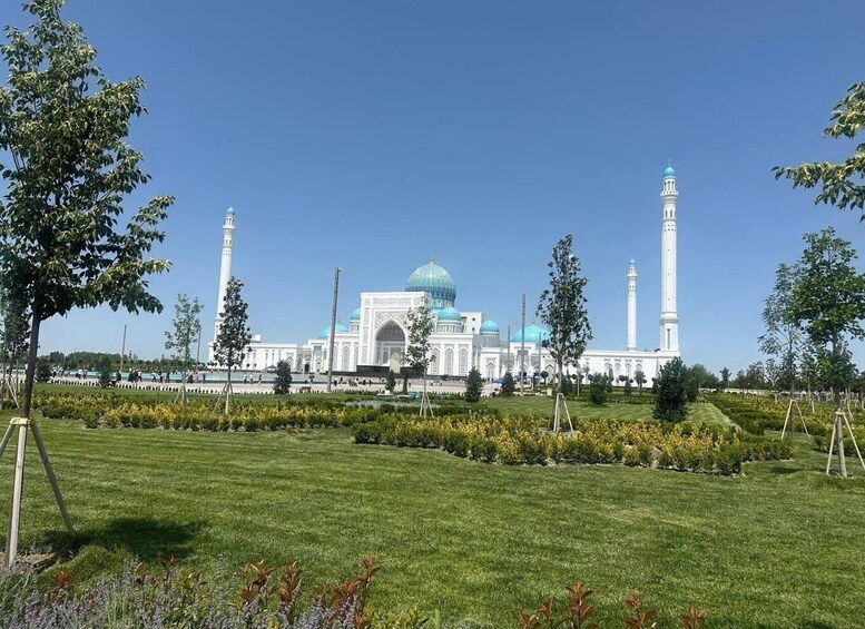A large white mosque with blue domes and minarets, surrounded by a well-maintained garden. 5