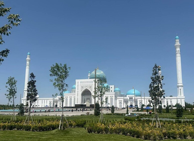 A large white mosque with blue domes and minarets, surrounded by a well-maintained garden. 5
