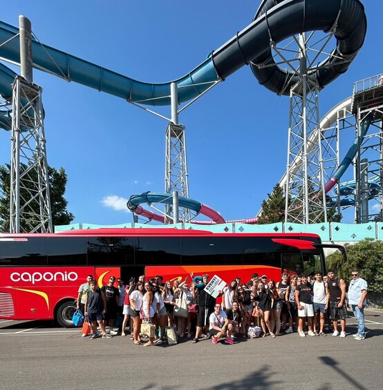 A group of people standing in front of a red bus with the 'caponio' logo, with a water park and tall structures in the background. 3