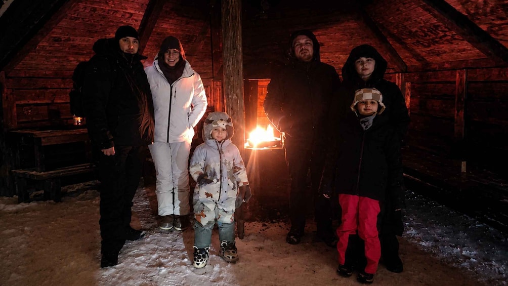 A group of people in a wooden, vaulted room with a fire burning in the background. 2