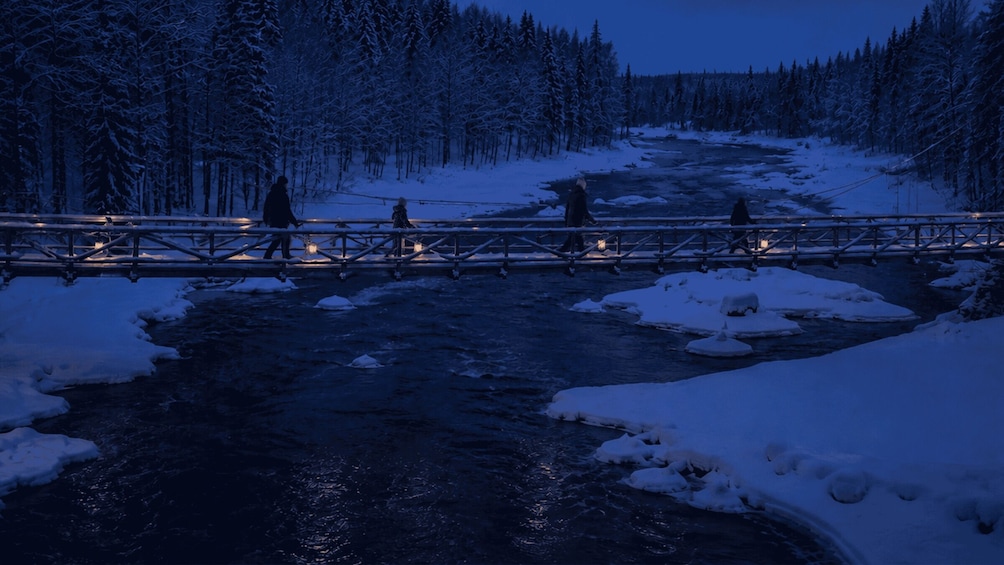 A snow-covered river with a wooden bridge and trees in the background. 5
