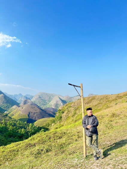 A person standing on a grassy hill with a wooden signpost, surrounded by green hills and a clear blue sky. 4