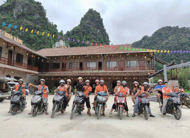 A group of people on motorcycles in front of a building with a stone facade and a balcony, surrounded by greenery and mountains. 2