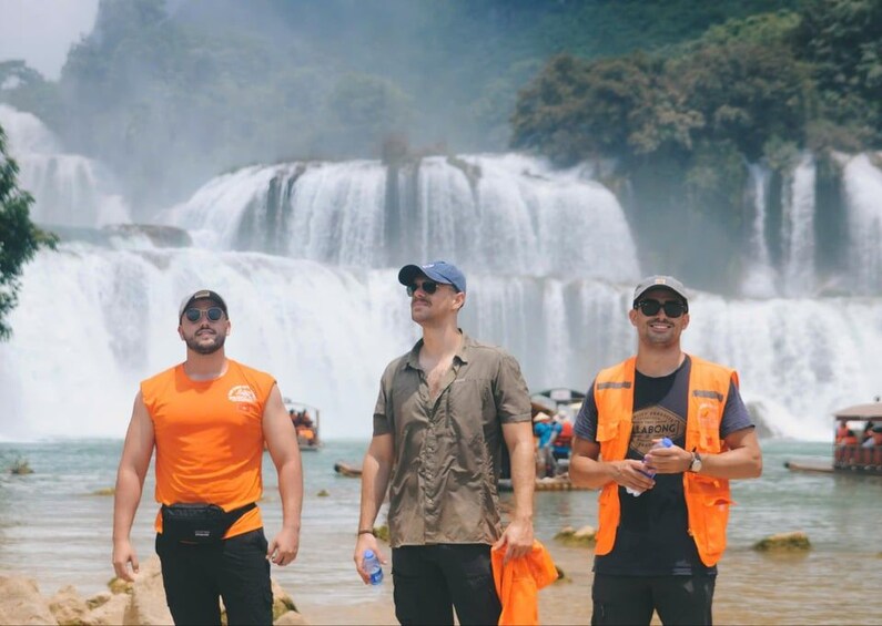Three people walking near a waterfall with boats in the background. 4