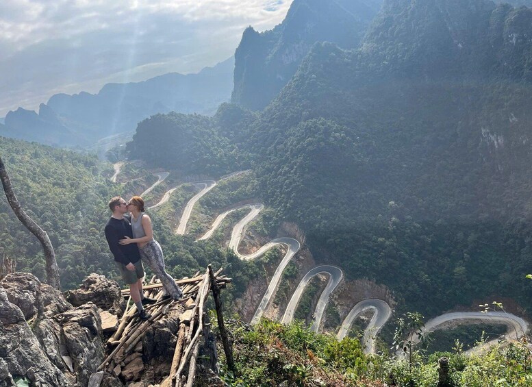 A couple embracing on a rocky outcrop overlooking a winding mountain road. 2