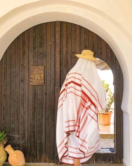 A person standing in front of a wooden door with a striped garment and a straw hat. 1