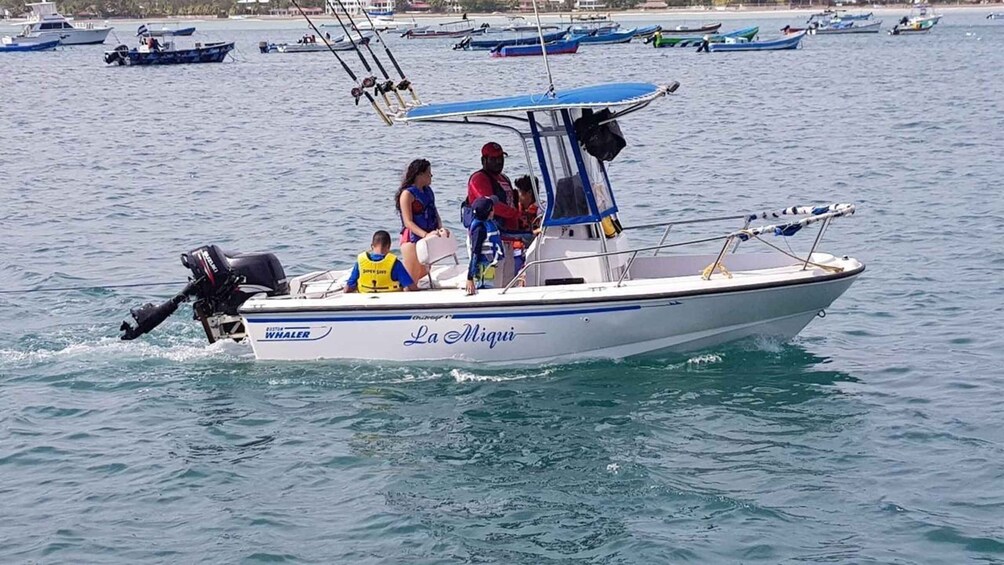 A boat named 'La Miqui' with people on board, moving through calm waters with other boats in the background. 2