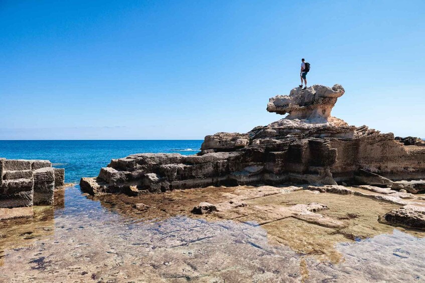 A person standing on a rock formation by the sea. 2