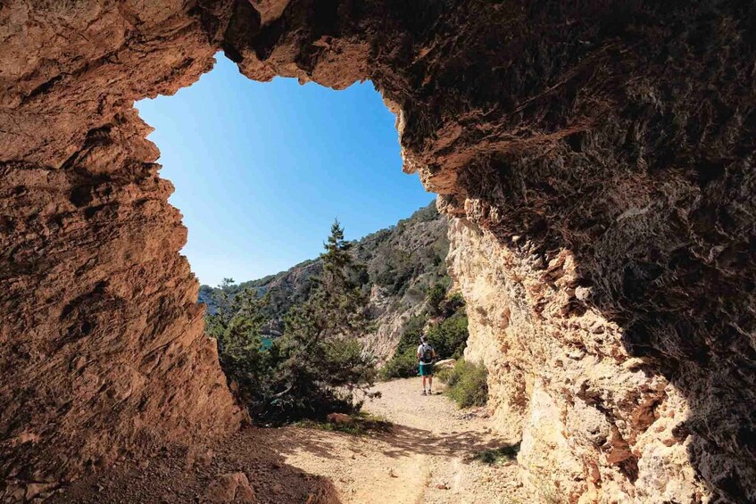 A rocky path through a natural arch formation with a hiker in the distance. 4