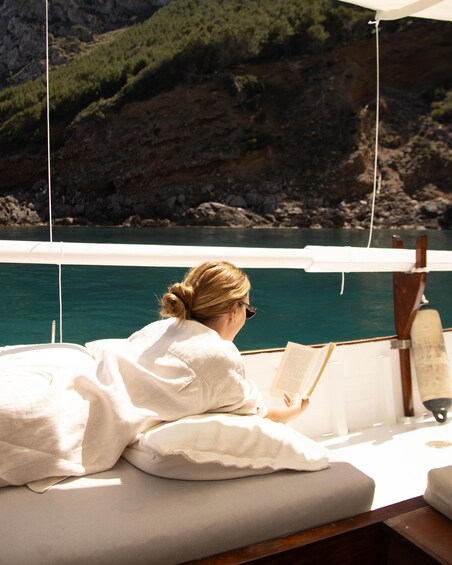 A person reading a book on a boat with a rocky coastline in the background. 3
