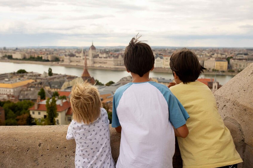 Three children looking at a cityscape with a river and a prominent tower. 1