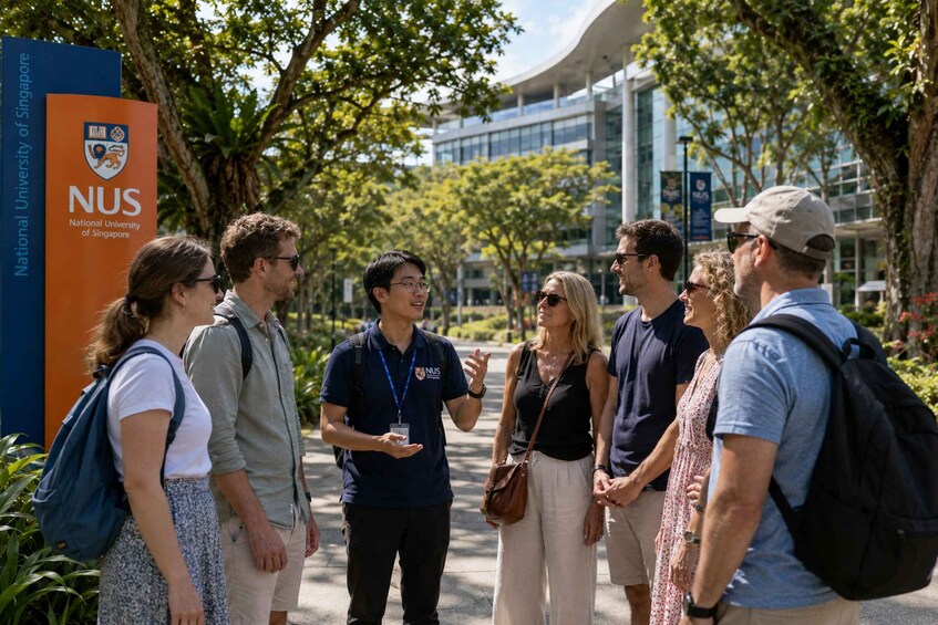 A group of people standing outdoors near a building with a sign for the National University of Singapore. 3
