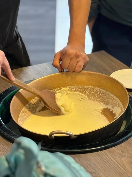 A person stirring a yellow mixture in a pan on a stove. 1